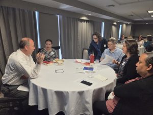 Conference attendees sit at a round table in discussion