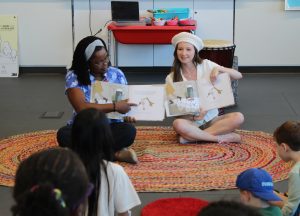 Two women reading a story to children during CISH