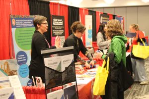 Andrea Fowler and Essie Lenchner talk to a K-12 educator at the WIRC table at the WCSS